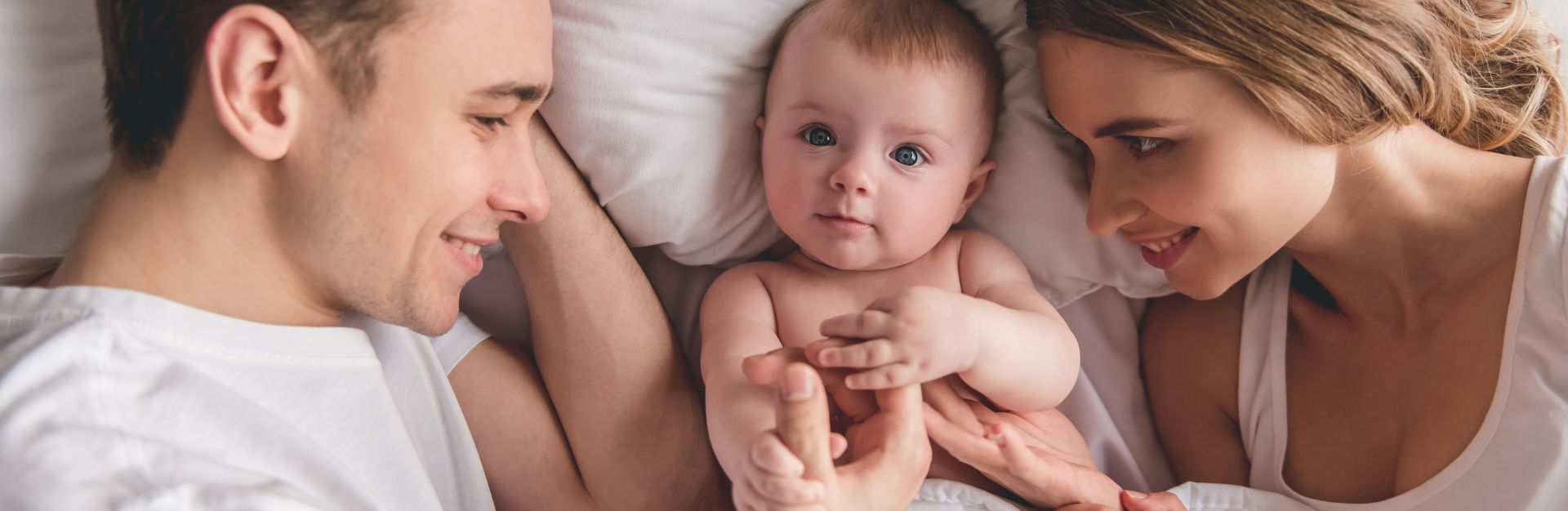 szczęśliwa para leżąca z niemowlakiem na łóżku poczętym metodą in vitro